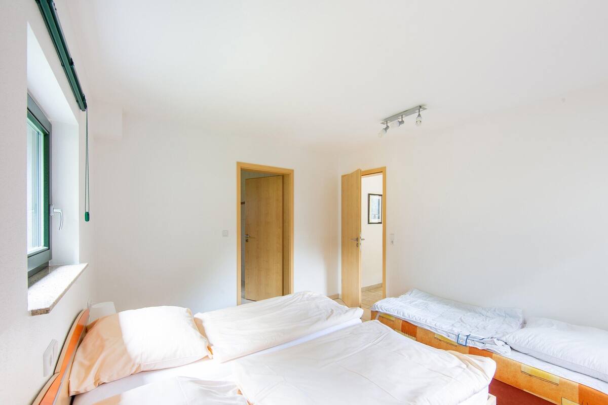 A bedroom with two beds, a window, and a door.