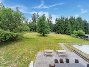 A patio with picnic tables and chairs, a grassy yard, and a forested area in the background. - Spacious Semi-detached House With Wood Stove Located Directly on the Rennsteig (Eisfeld)