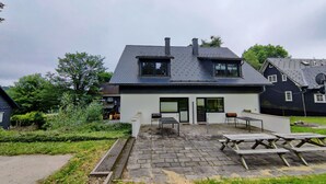 A modern house with a sloped roof, a paved patio, and a small outdoor seating area. - Spacious Semi-detached House With Wood Stove Located Directly on the Rennsteig (Eisfeld)