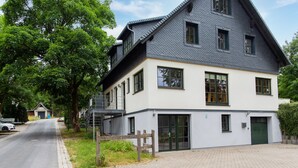 A two-story building with a balcony, a garage, and a paved driveway. - Spacious Semi-detached House With Wood Stove Located Directly on the Rennsteig (Eisfeld)