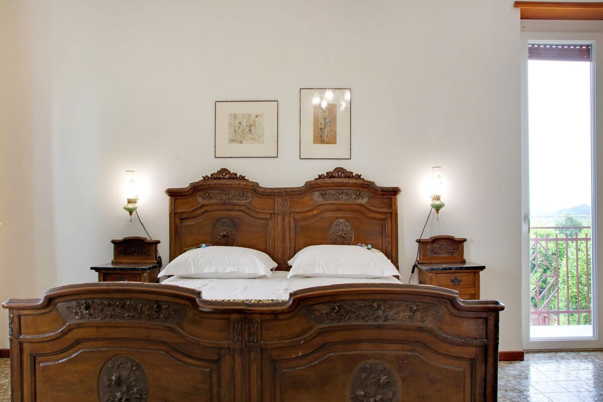 Un letto di legno con elaborate decorazioni intagliate, due lampade fissate al muro e due quadri appesi sopra.