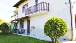 A two-story building with a balcony, a small porch with chairs, and a well-maintained lawn.