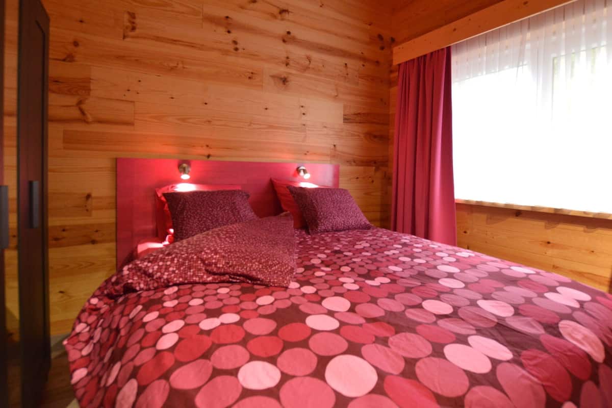 Ein Schlafzimmer einer Holzhütte mit einem Bett, zwei Nachttischlampen und einem Fenster mit Vorhängen.