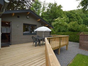 A modern wooden deck with a table and chairs, a white umbrella, and a wooden railing.