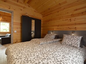 A bedroom with a wooden ceiling, a bed with patterned bedding, a wardrobe, and a chair.
