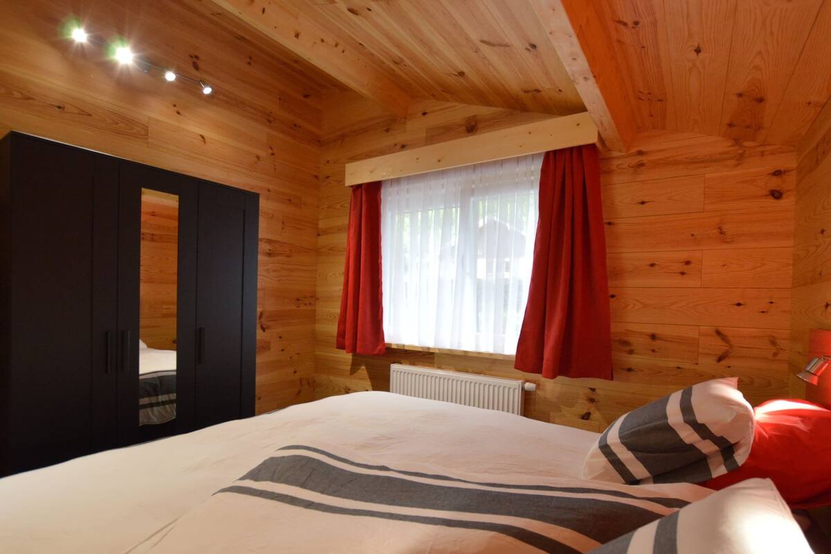 Ein Holzhütten-Zimmer mit einem Bett, einem Fenster mit roten Vorhängen und einer Heizung.