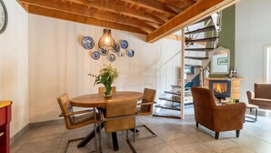 Un comedor con una mesa de madera, sillas y un florero. Se observa una escalera de caracol al fondo que conduce a otra habitación.