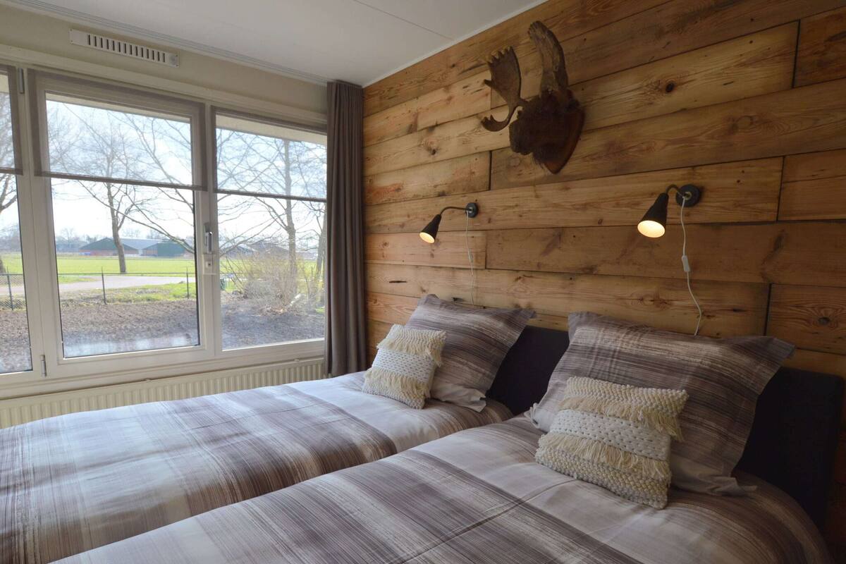 A bedroom with two beds, a wooden headboard, a mounted animal skull, and a window with a view of a park.