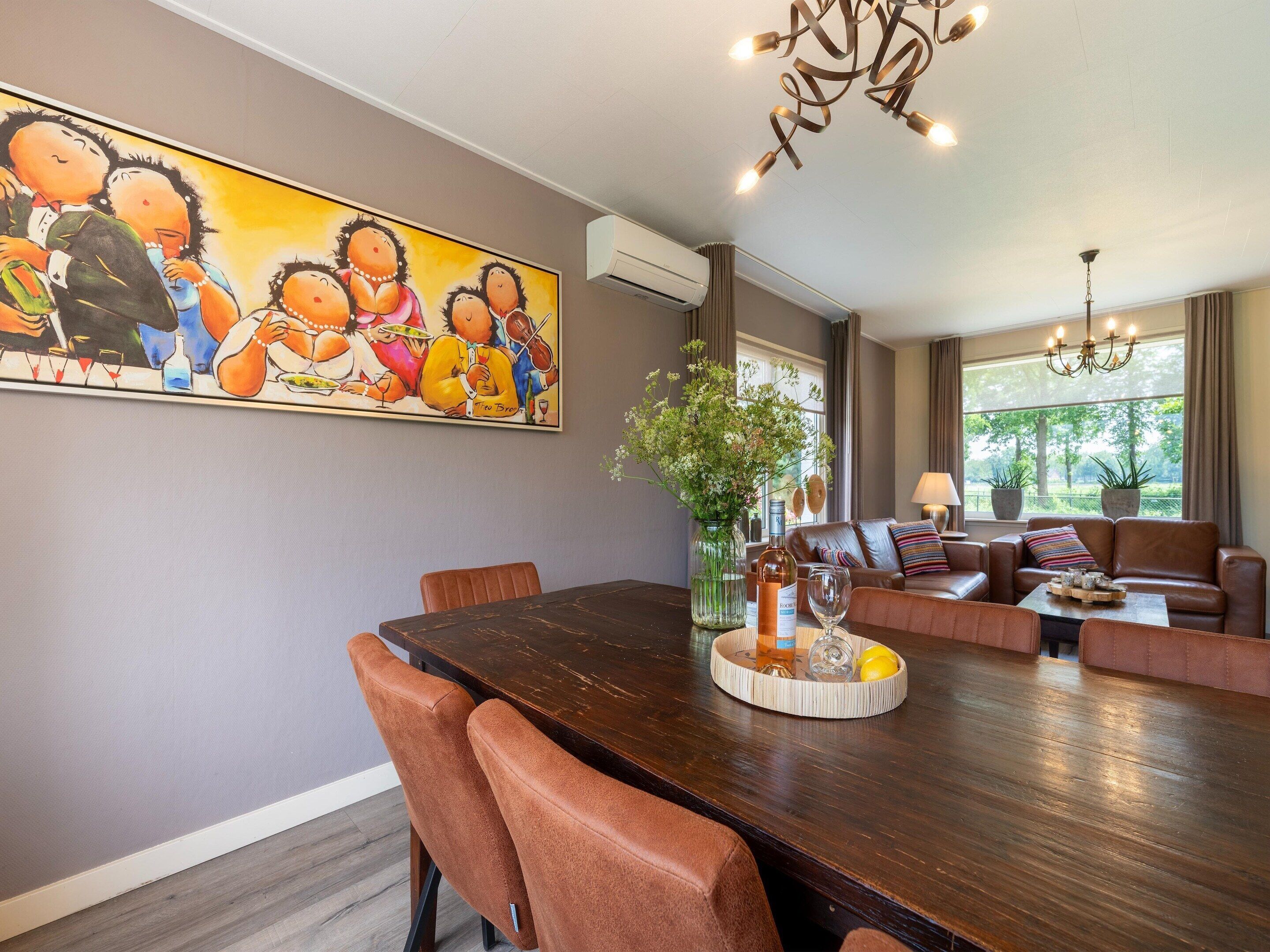 Un espace repas avec une longue table en bois, des chaises à revêtement marron et un grand tableau accroché au mur.