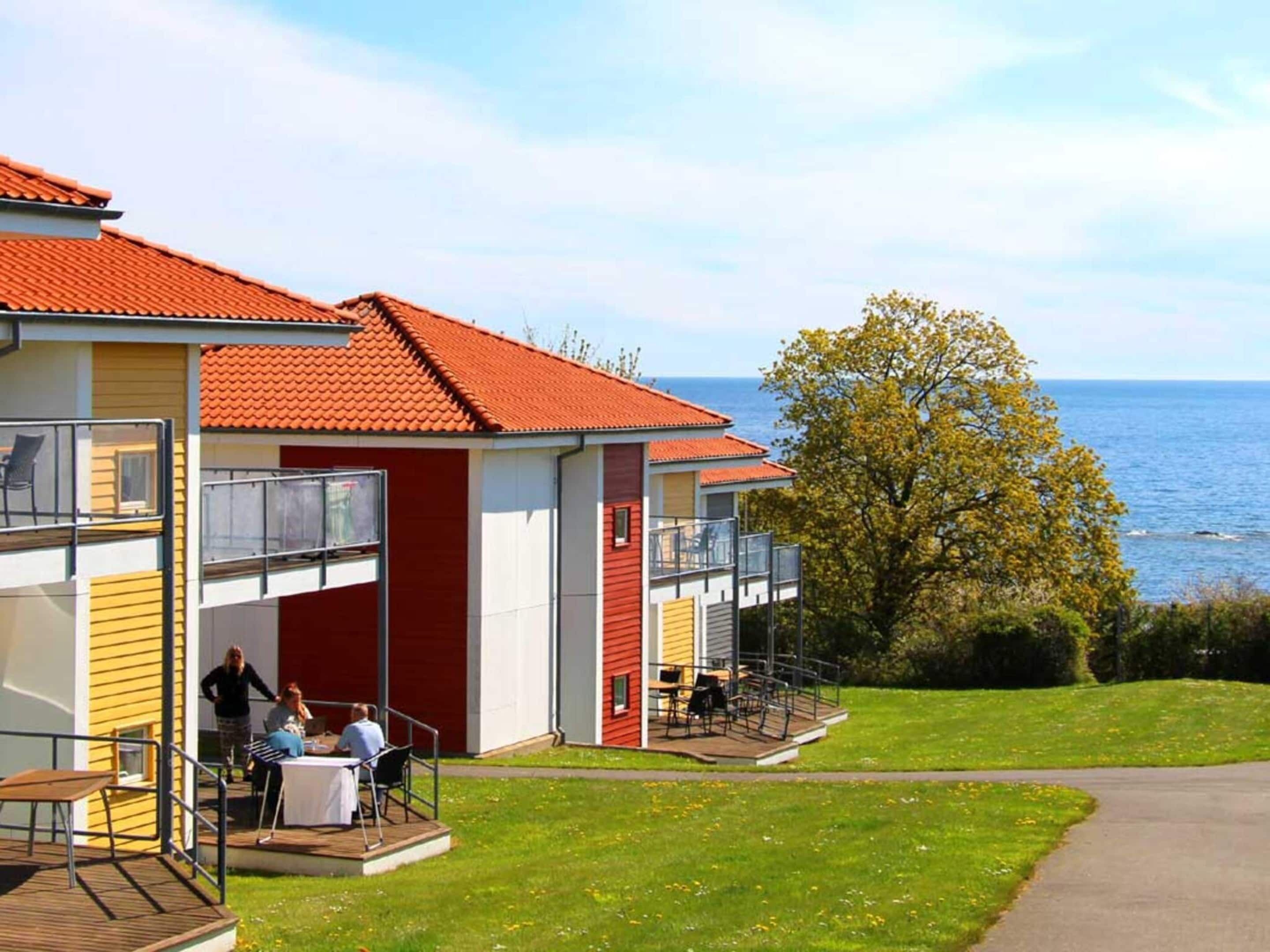 A coastal building with a red roof, a balcony, and a view of the sea.