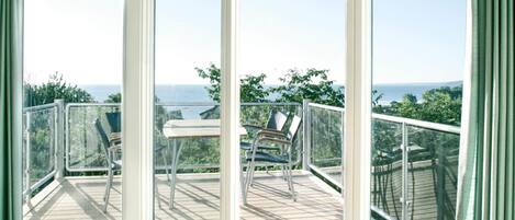 A balcony with a table and chairs, overlooking a scenic view of the sea.