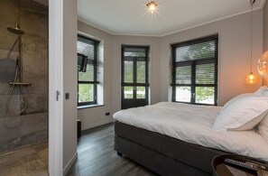 A modern bedroom with a large bed, a shower, and three windows with blinds. - Attractive Apartment in Domburg With Balcony (Domburg)