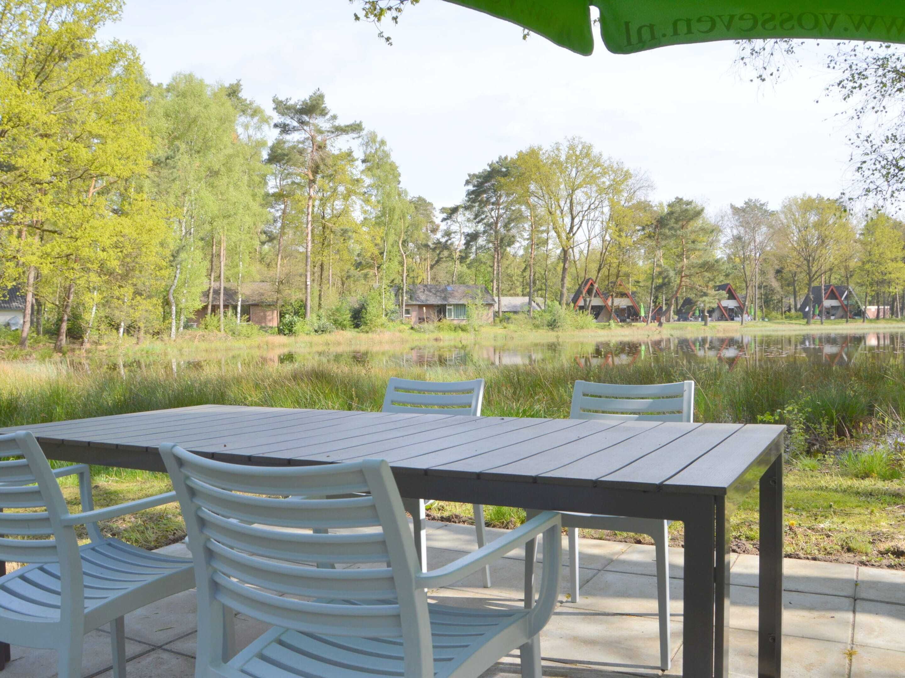 A table with chairs outside near a body of water, surrounded by trees and buildings.