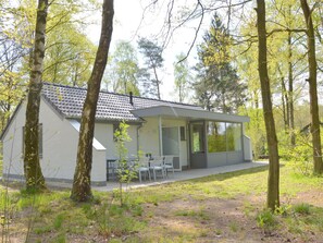 A modern house with a tiled roof, a covered patio with chairs, and a grassy yard surrounded by trees. - Alluring Holiday Home in Limburg Near Forest (Stramproy)