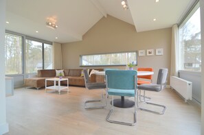 A spacious living room with a high ceiling, a large window, and a modern seating arrangement including a sofa, chairs, and a small table. - Alluring Holiday Home in Limburg Near Forest (Stramproy)