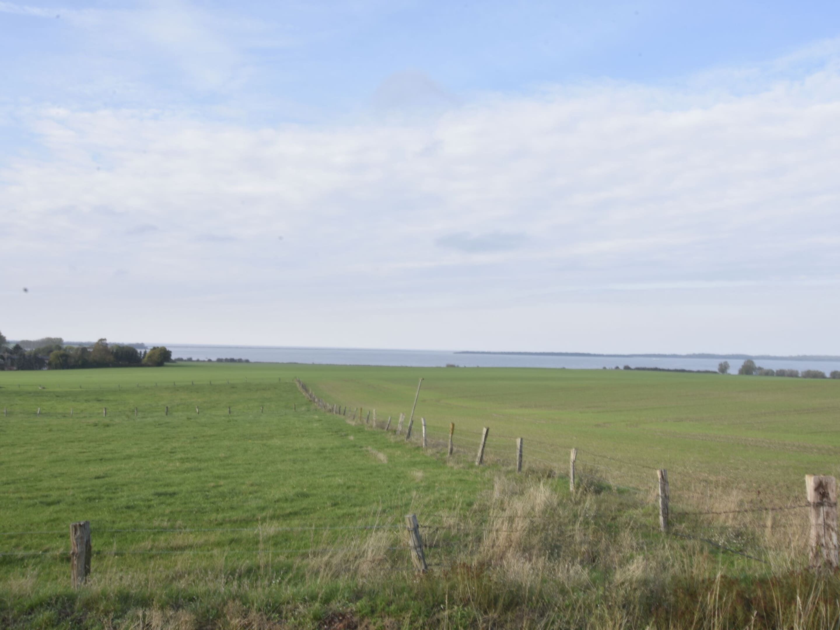 A wide-open field with a fence running through it, leading to a body of water in the distance.