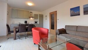 A modern living room with a glass coffee table, a red armchair, and a grey sofa. There is a kitchen in the background with white cabinets and a microwave. - Modern Holiday Home in Boiensdorf Near Sea (Boiensdorf)