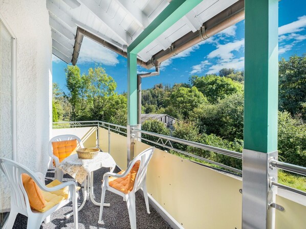 A balcony with a table and chairs, overlooking a forested area. - Modern Apartment in Schwalefeld With Garden (Willingen)