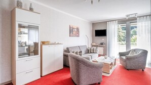 A modern living room with a red carpet, grey sofas, a white cabinet, and a TV mounted on the wall. - Modern Apartment in Schwalefeld With Garden (Willingen)