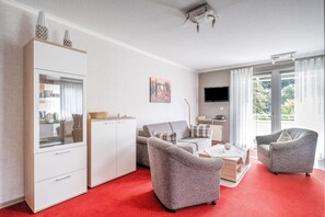 A modern living room with a red carpet, grey sofas, a white cabinet, and a TV mounted on the wall. - Modern Apartment in Schwalefeld With Garden (Willingen)