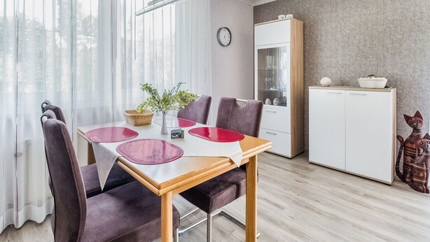A dining area with a table, chairs, a vase with greenery, and a cabinet with kitchenware. - Modern Apartment in Schwalefeld With Garden (Willingen)