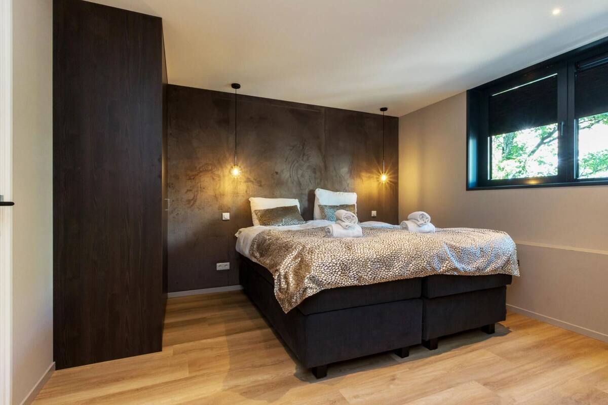 A modern bedroom with a large bed, dark wood paneling, and two pendant lights.