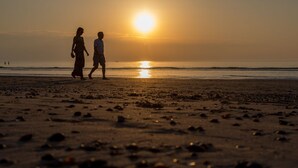 A beach scene with two people walking, the sun setting in the background. - Appealing Apartment in Domburg Near the Beach (Domburg)