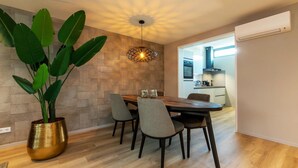 Un comedor moderno con una mesa de madera, cuatro sillas, una planta verde grande en una maceta dorada y una lámpara de techo original.