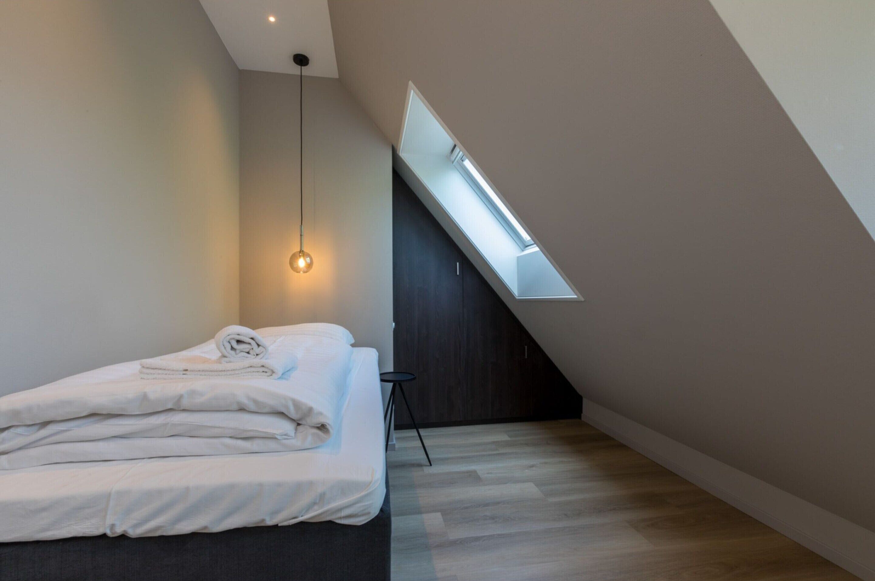 Een moderne slaapkamer met dakraam, een opgemaakt bed en een hanglamp.