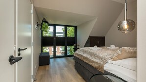 A modern bedroom with a large bed, a desk, and a view of the outdoors. - Appealing Apartment in Domburg Near the Beach (Domburg)