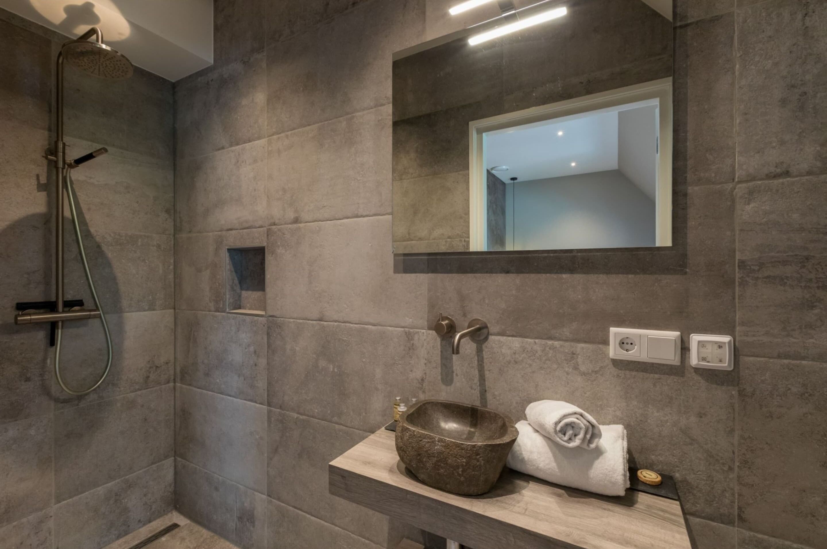 Une salle de bain moderne avec un lavabo en pierre, une douchette à main et un miroir au-dessus du lavabo.