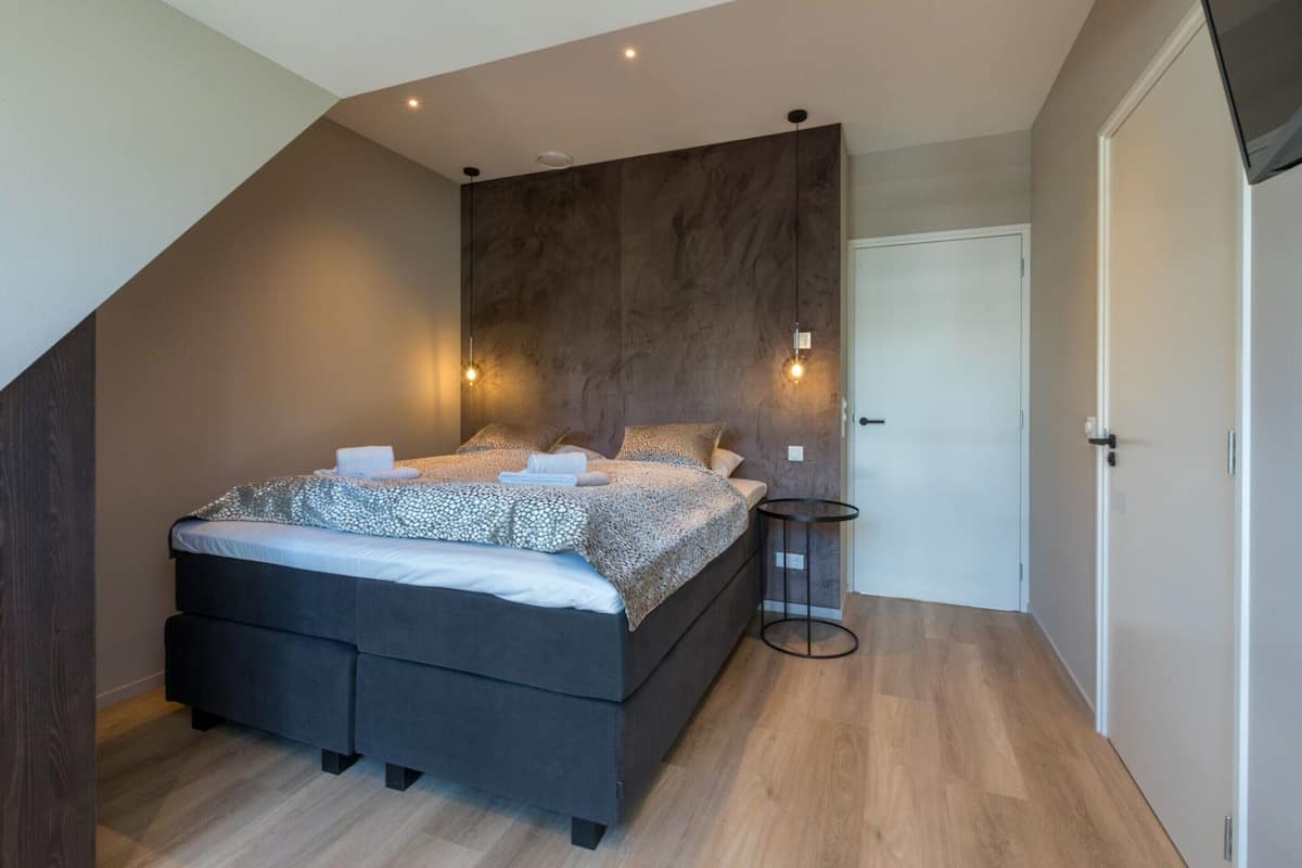 A modern bedroom with a large bed, a small bedside table, and a built-in wardrobe.