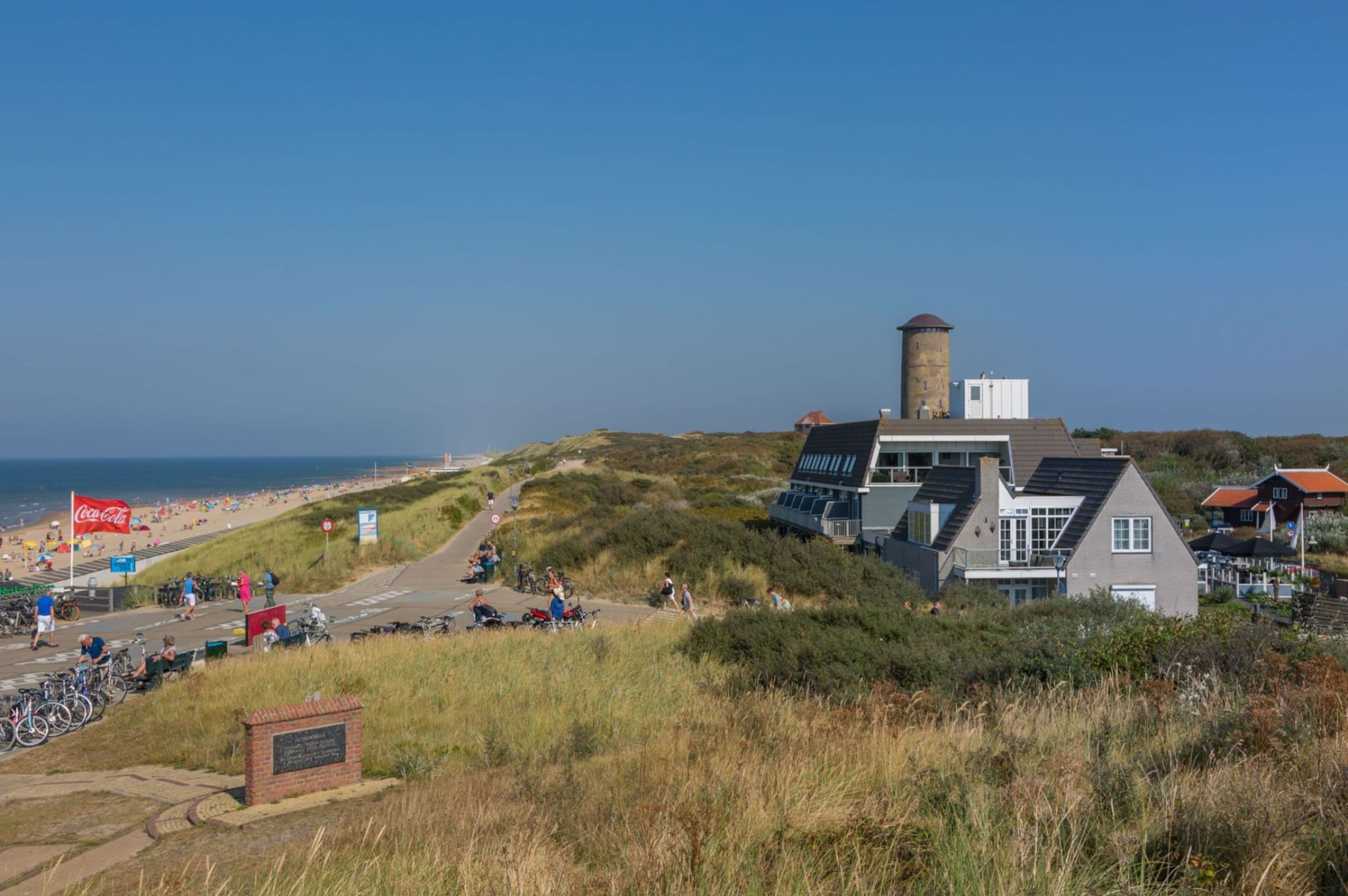 A coastal building with a prominent tower, a beach in the background, and a clear sky.