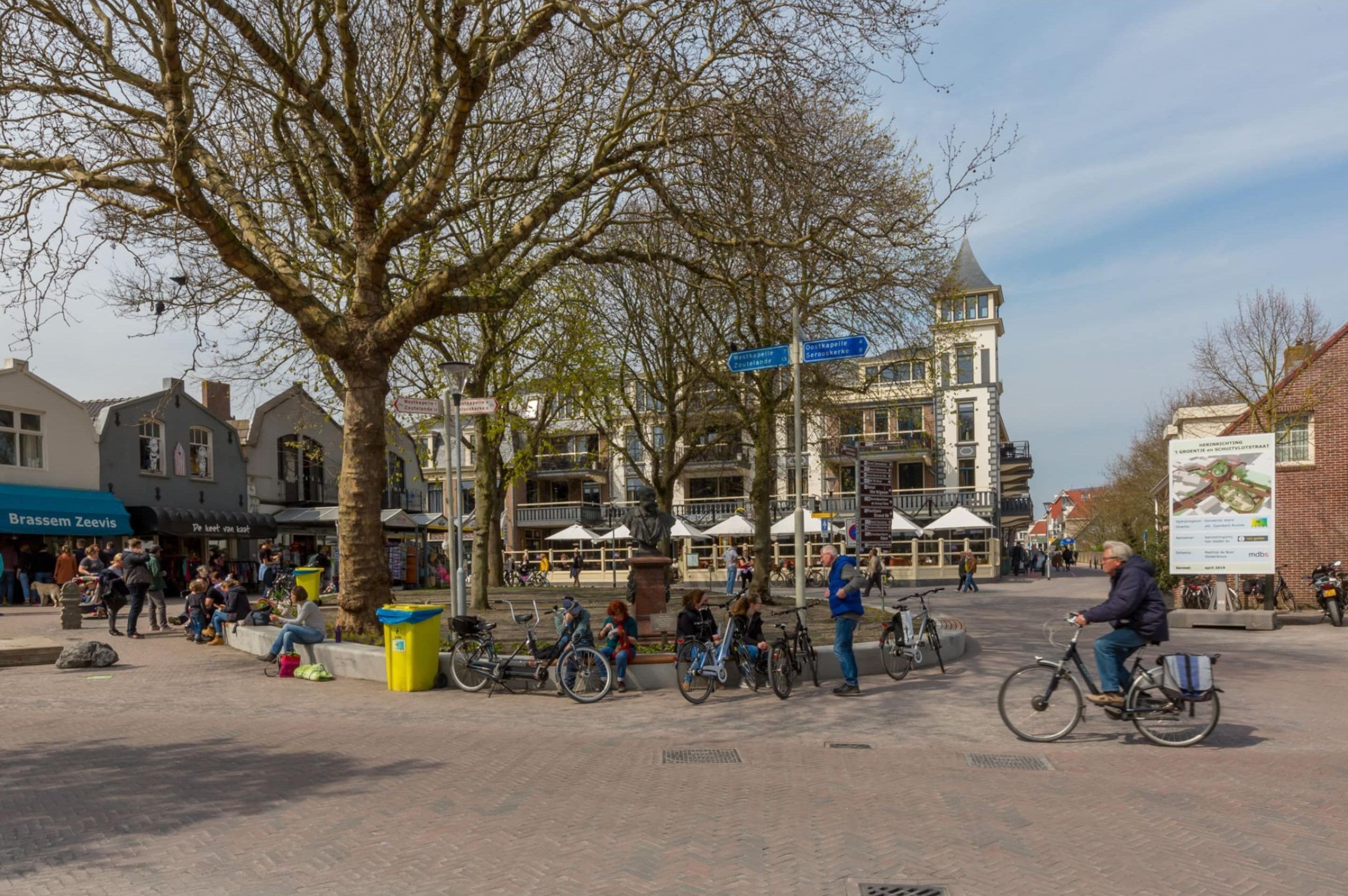 A public square with a large tree, bicycles, and people.
