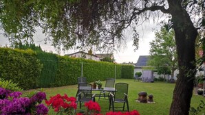 A garden with a table and chairs, surrounded by hedges and flowering plants. - Comfortable Apartment Near Insel Poel (Blowatz)