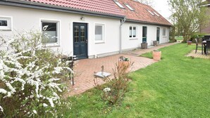 A single-story house with a red-tiled roof, a black front door, and a small garden area with a lawn and a few potted plants. - Lovely Apartment in Stellshagen With Garden (Damshagen)