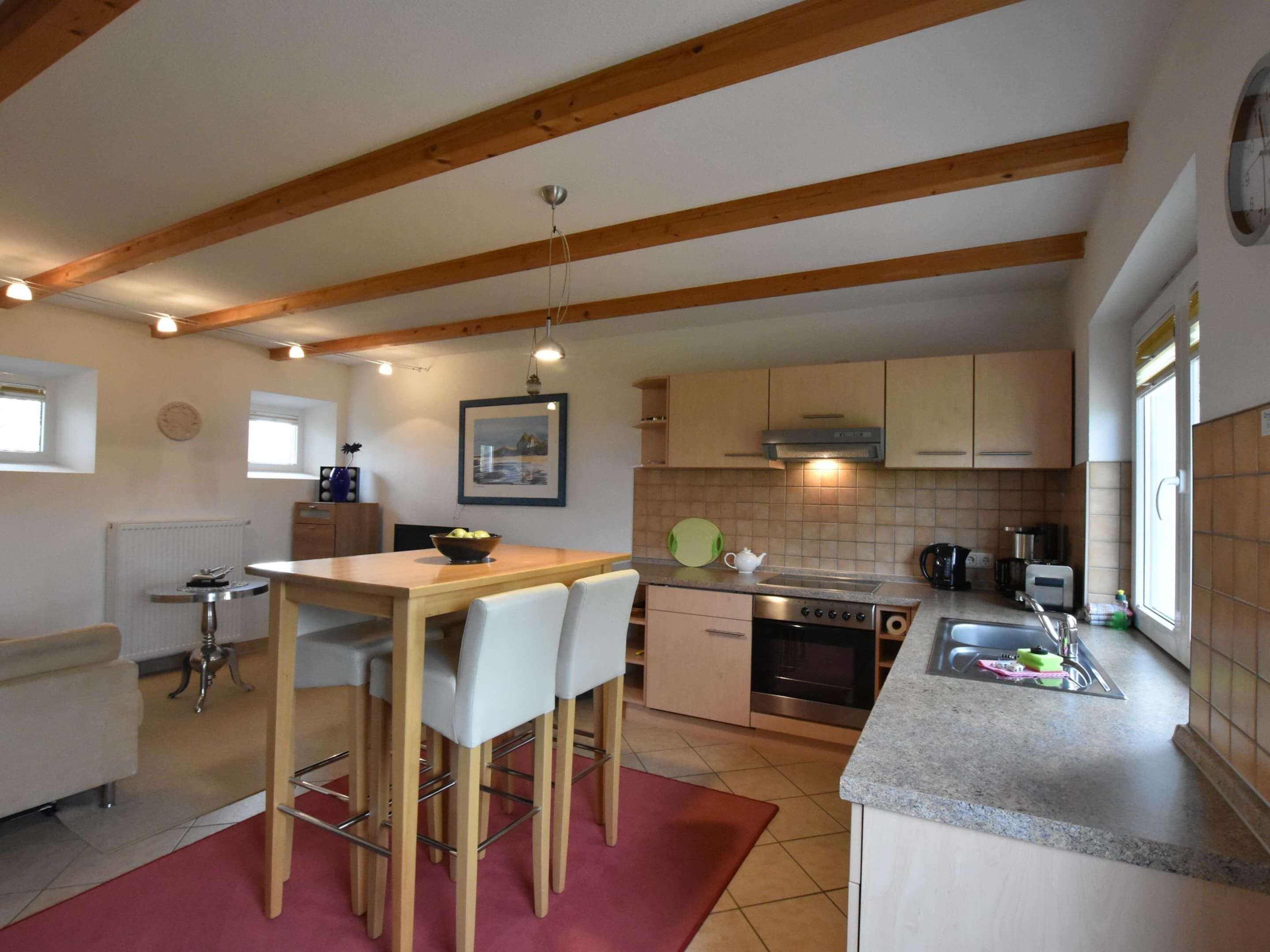 A kitchen with wooden beams, a dining table with chairs, a stove, and a sink.