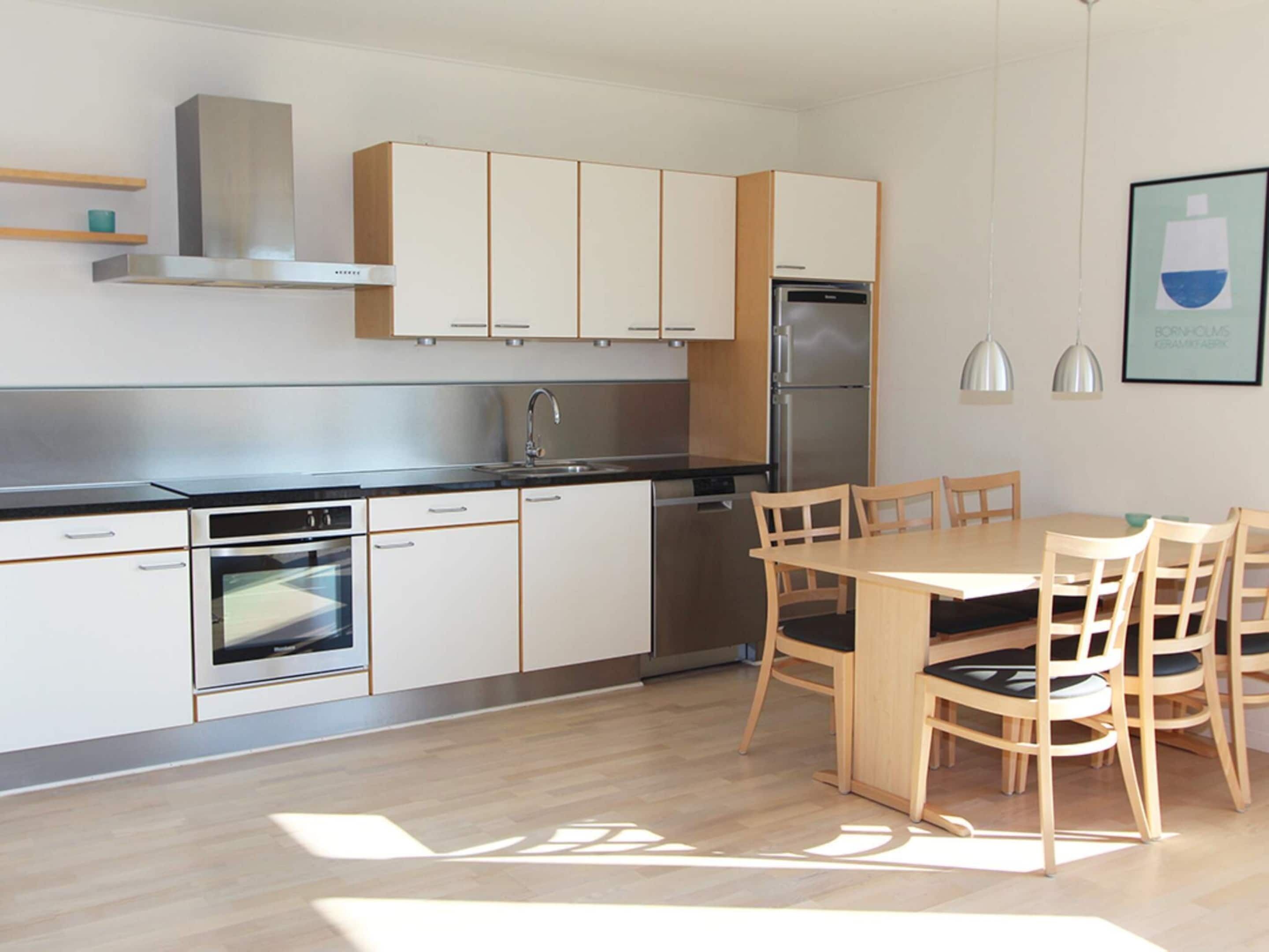 A modern kitchen with white cabinets, stainless steel appliances, and a wooden dining table with chairs.