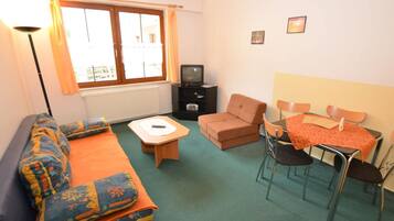 A compact living room with a sofa, a small table, a TV, and a dining area with chairs.