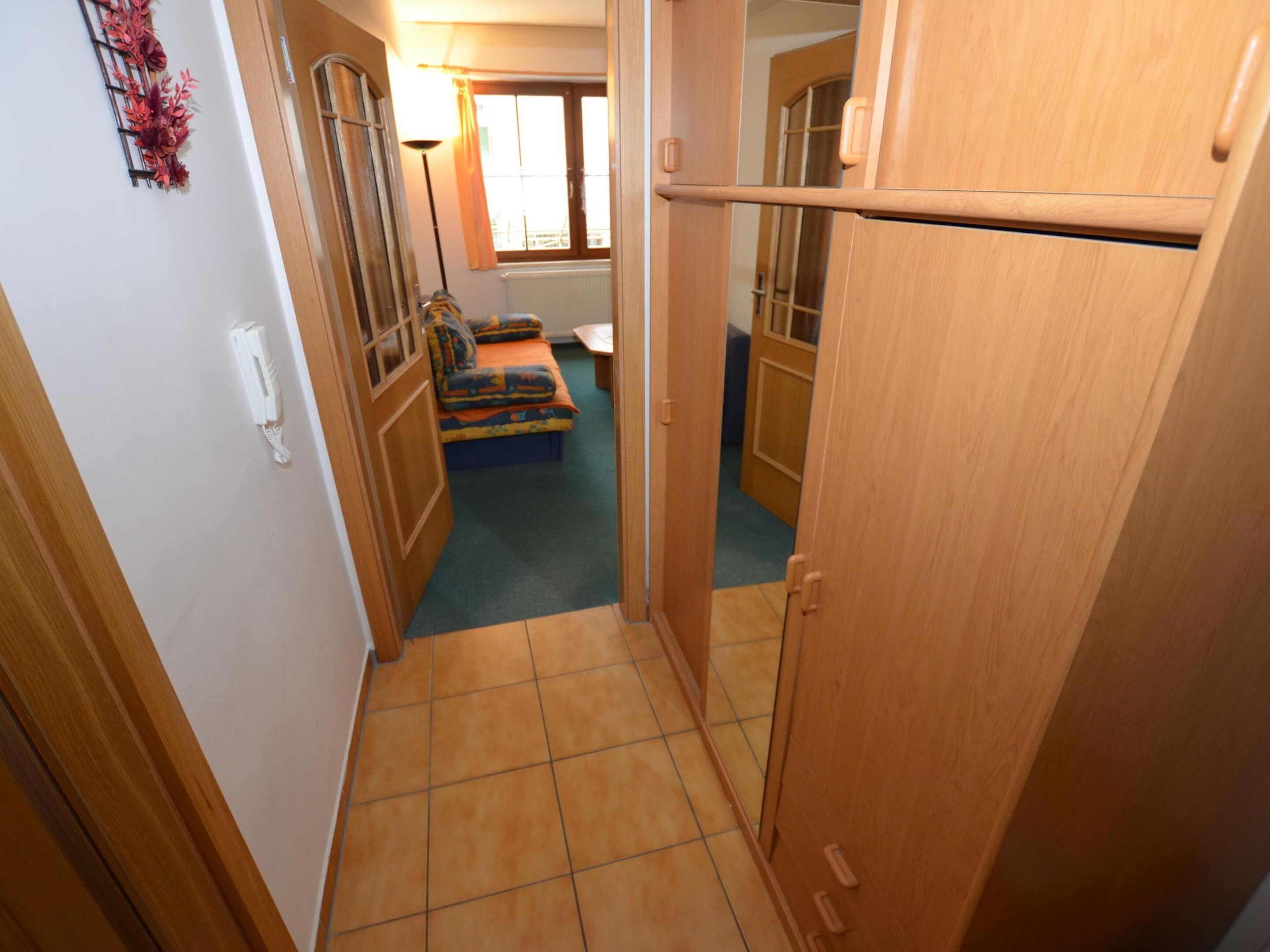 A narrow hallway with a wooden door, a small seating area with a colorful cushion, and a radiator in the background.