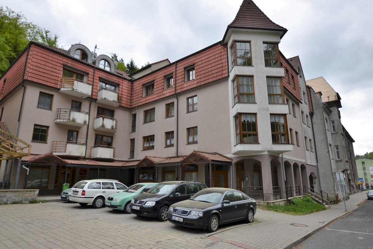 A multi-story building with a red-tiled roof, multiple balconies, and a parking area with several cars.