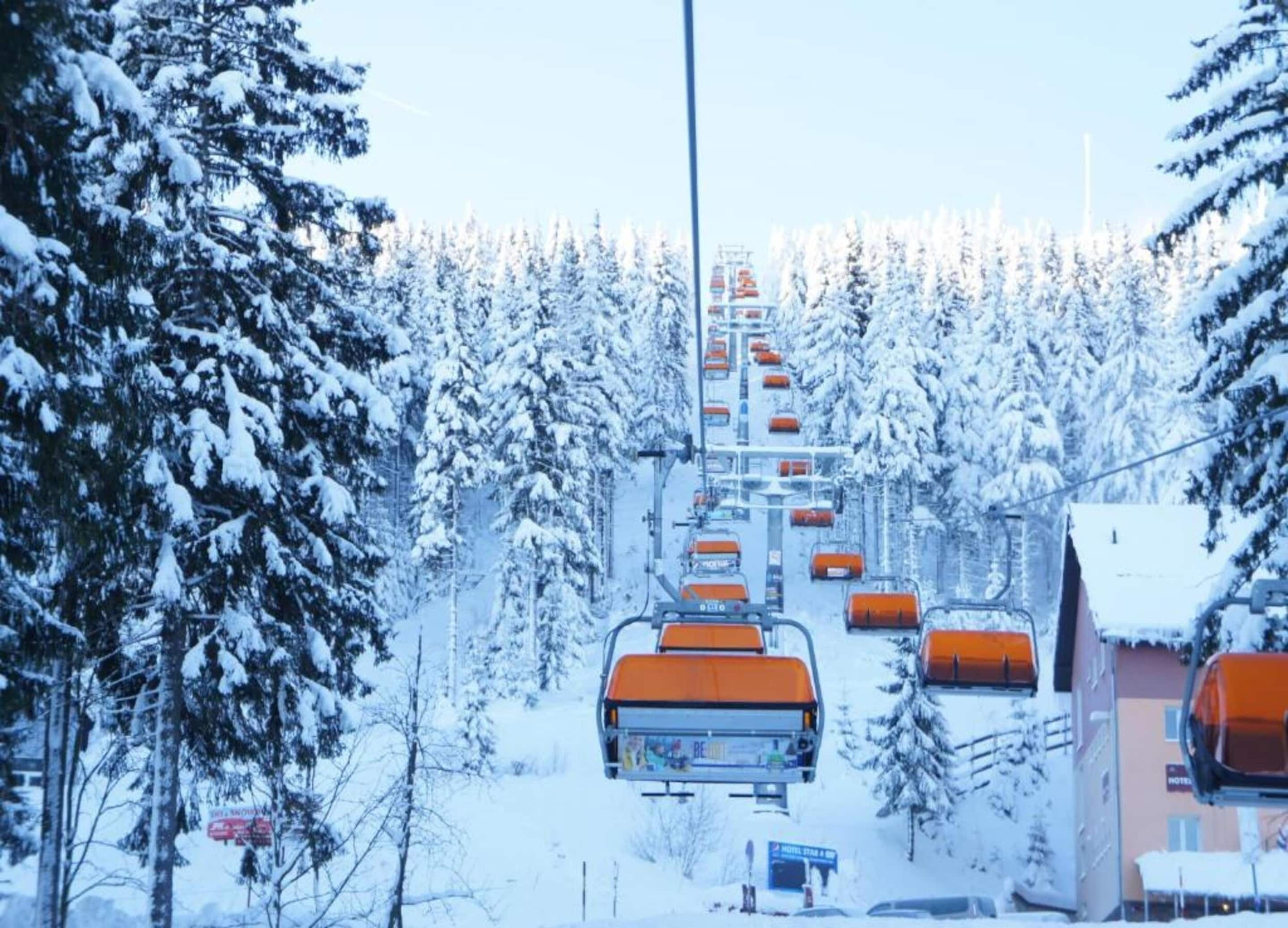 Un telesilla con cabinas naranjas, rodeado de árboles nevados y edificios.
