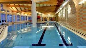En indendørs swimmingpool med tydelige baner, en rød rutsjebane og udsigt til himlen gennem store vinduer.