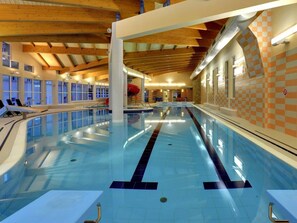 Piscina interior com pistas demarcadas, um escorrega vermelho e vista para o céu através de amplas janelas.