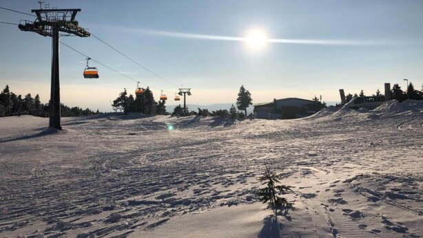 En skibakke med svævebane, en klar himmel og et solbelyst landskab.