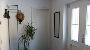 A hallway with a potted plant, a hat on a rack, and a door with a mirror. - Cosy Apartment in Weissig With Garden (Struppen)