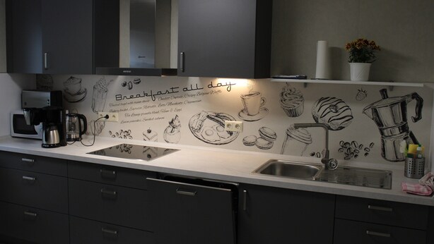 A modern kitchen with dark cabinets, a white countertop, and a wall mural depicting breakfast items. - Cosy Apartment in Weissig With Garden (Struppen)