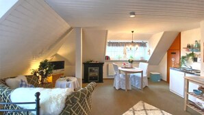 Un espace de vie chaleureux aménagé dans les combles, comprenant un canapé, une table à manger et un coin cuisine.