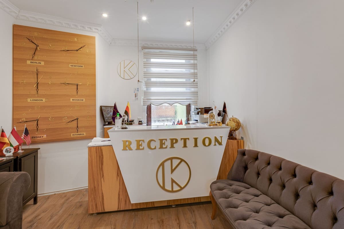 Un mostrador de recepción con un panel de madera que muestra nombres de ciudades y un gran logotipo 'K'.