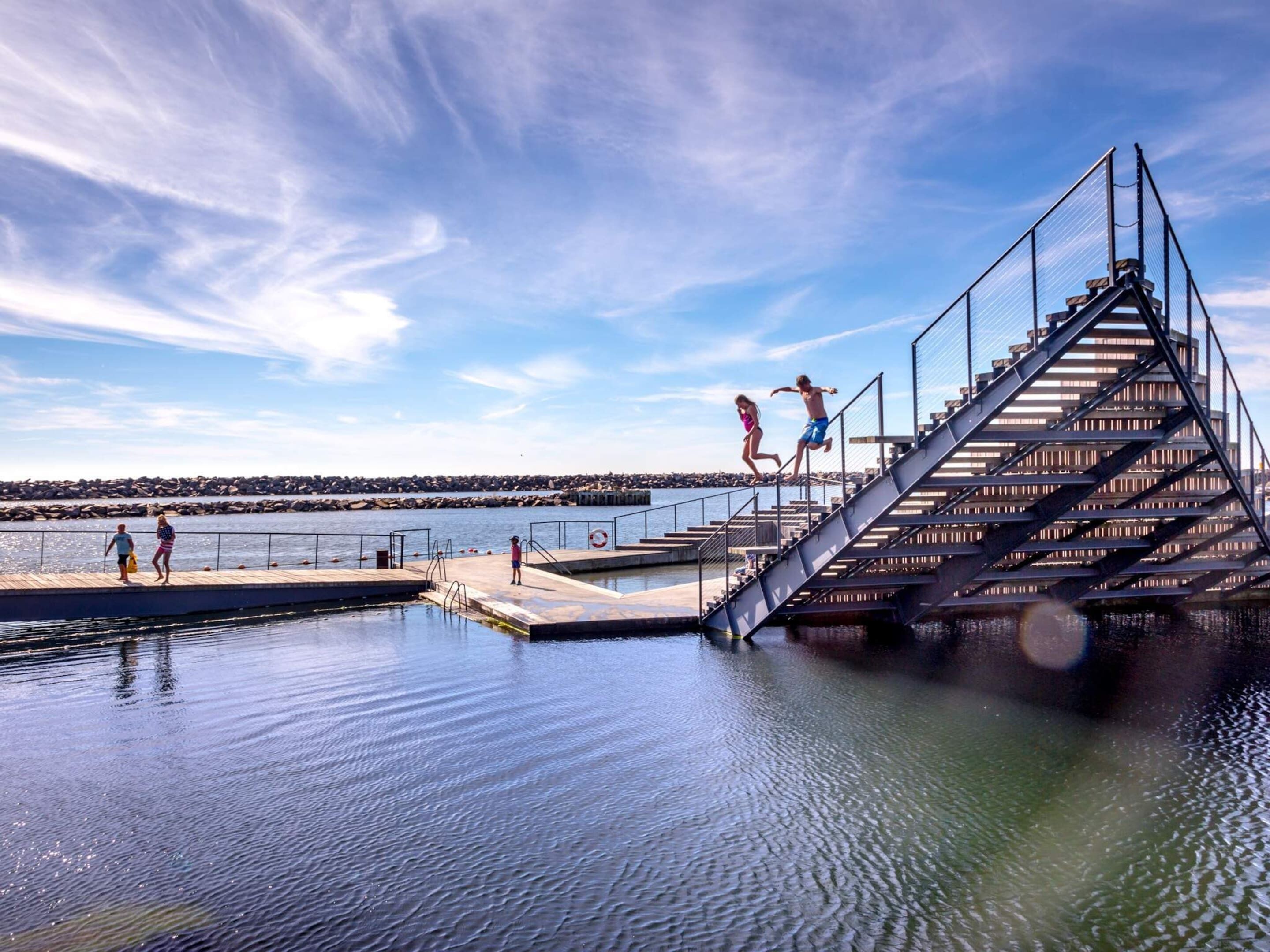 A waterfront pier with a staircase leading into the water, a calm sea, and a clear sky.